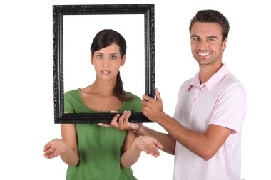 Playful couple stood with empty picture frame clipart