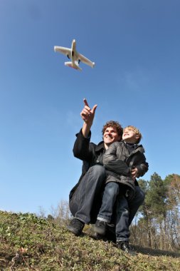 Father and son playing with toy plane in field clipart