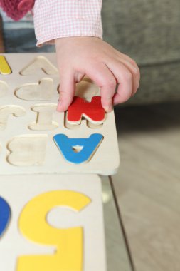 Kid playing with wooden letter puzzle clipart