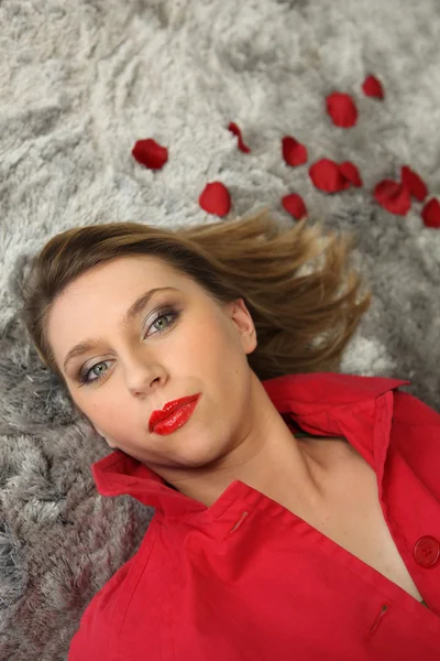 Женщина, лежащая на ковре рядом с лепестками роз — стоковое фото