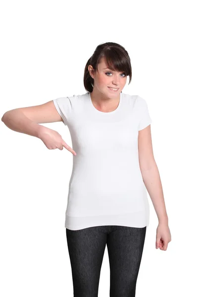 Молодая женщина указывает на свою простую белую футболку — стоковое фото