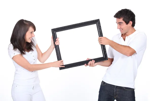 Couple fighting over blank picture frame — Stock Photo, Image