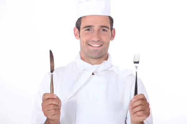 Chef de uniforme segurando uma faca e garfo — Fotografia de Stock