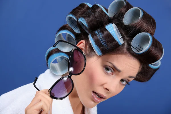 Mulher com o cabelo em rolos segurando um par de óculos de sol — Fotografia de Stock