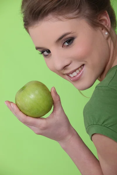 Молодая девушка ест яблоко на зеленом фоне — стоковое фото