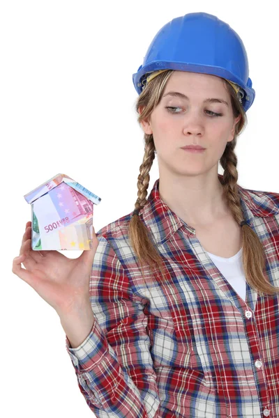 Craftswoman holding een kleine model van huis gemaakt van bankbiljetten — Stockfoto