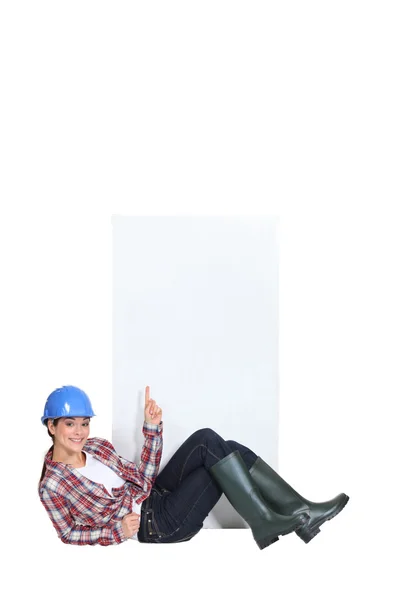 A female construction worker pointing at a blank poster. — Stock Photo, Image