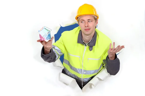 Confused builder holding house made from money — Stock Photo, Image