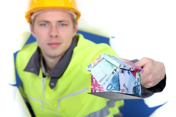 Un bricoleur présentant une maison miniature faite de billets en euros . — Photo