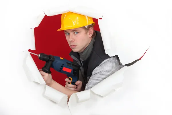 Craftsman holding a drill and breaking a paper wall — Stock Photo, Image