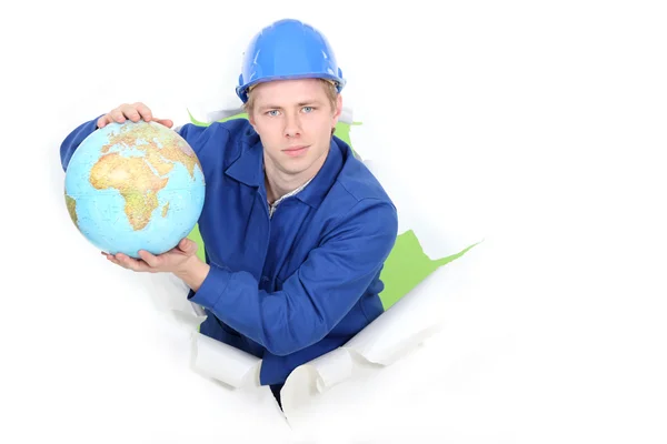 Handwerker posiert in einem Loch aus Papierwand und hält eine Weltkugel in der Hand — Stockfoto