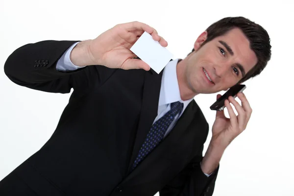 Empresário falando em seu telefone celular e segurando um cartão — Fotografia de Stock
