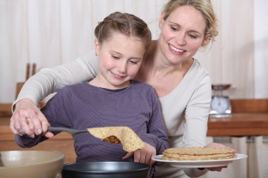 Mother and daughter making crepes together clipart