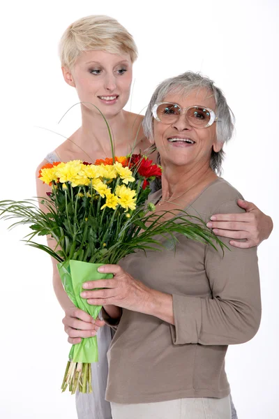 Young woman giving a senior lady a bunch of flowers — Stock Photo, Image