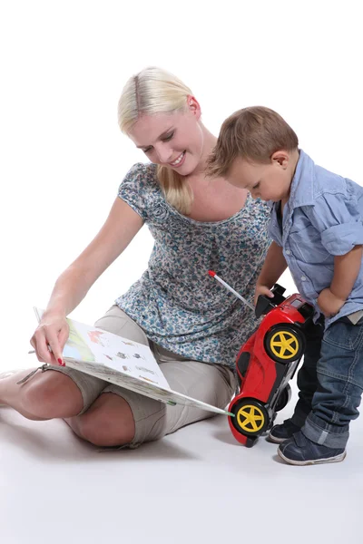 Мать показывает книгу своему маленькому мальчику, играющему с машиной — стоковое фото
