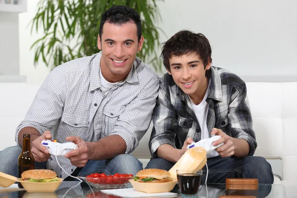 Vader en zoon spelen van videospelletjes en het eten van junkfood — Stockfoto