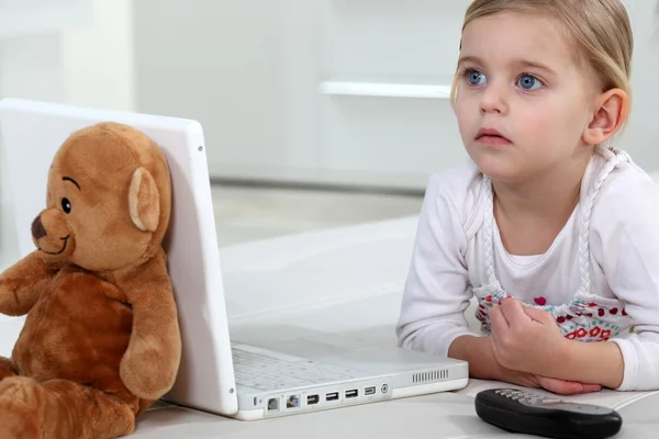 Kleines Mädchen liegt mit ihrem Teddy am Laptop — Stockfoto