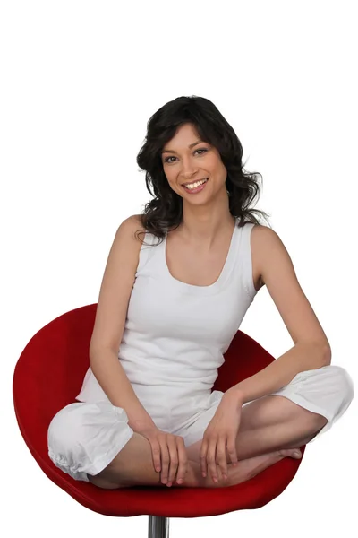 Woman in white sitting cross legged in a red chair — Stock Photo, Image