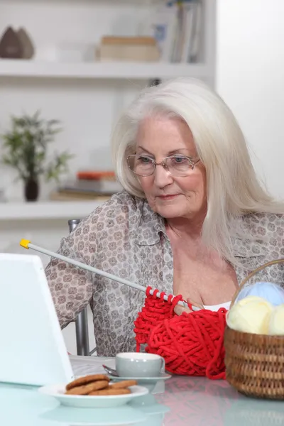 Elderly lady knitting by laptop — Stock Photo, Image