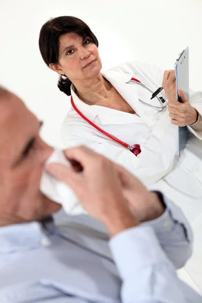 Doctor writing on a clipboard as her patient blows his nose — Stock Photo, Image