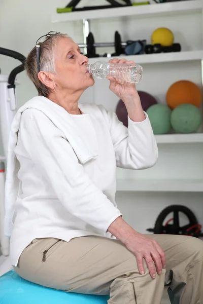 Oudere vrouw in de sportschool drinkwater — Stockfoto