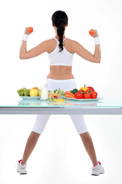 Mulher com halteres e pratos de salada e frutas — Fotografia de Stock