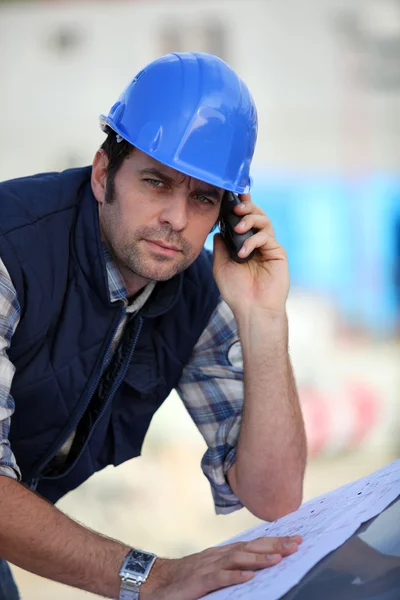 Foreman verificando planos enquanto no telefone — Fotografia de Stock
