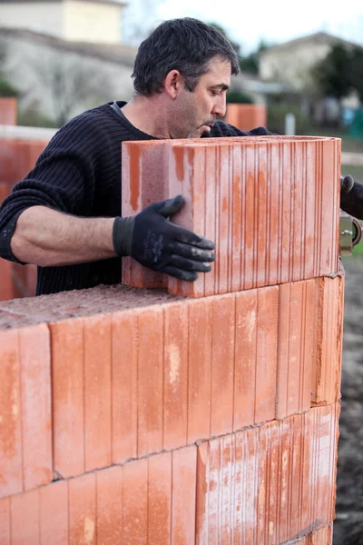 stock image Mason placing brick on unfinished wall