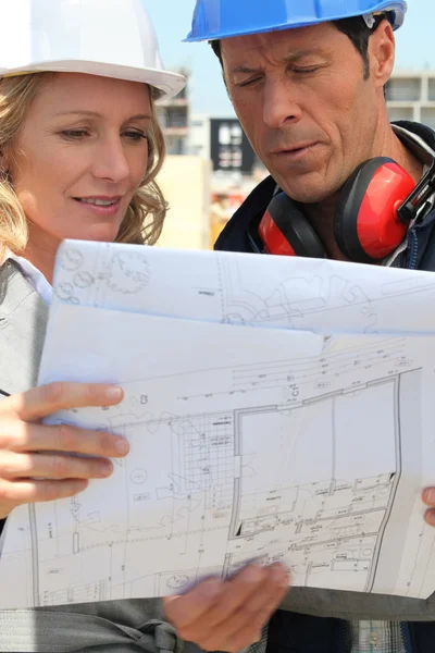 Female architect and workman consulting blueprints in construction site — Stock Photo, Image