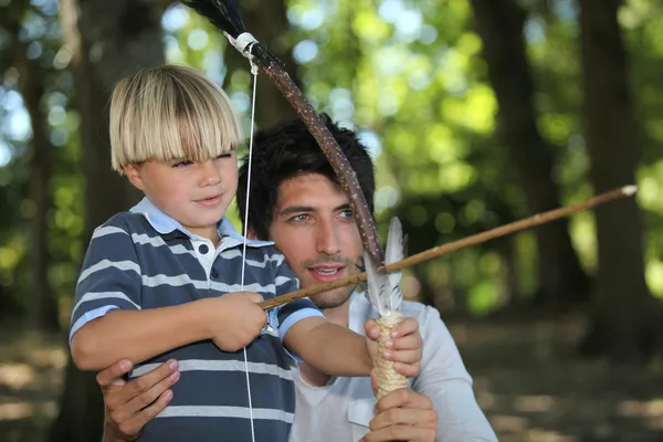 Чоловік і маленький хлопчик займаються стрільбою з лука в лісі — стокове фото