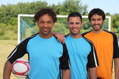 Three smiling footballers in front of goal clipart