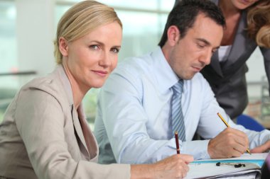 Businesswoman holding pen sat next to colleague clipart