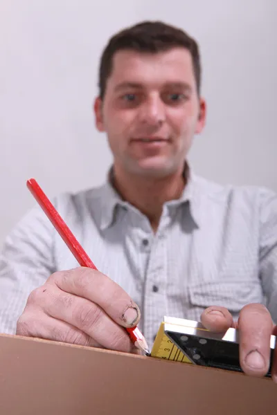 Closeup de um homem medindo um pedaço de madeira e marcando-o com um lápis — Fotografia de Stock