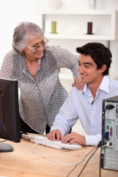 Молодой человек за компьютером и счастливая пожилая женщина — стоковое фото