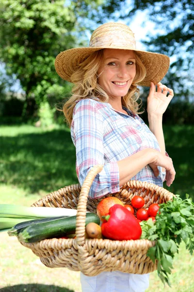 Jolie femme avec un chapeau de paille et un panier de légumes . — Photo