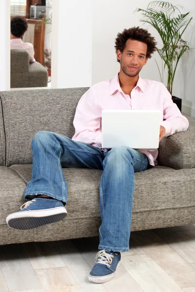 Άνθρωπος κάθεται σε έναν καναπέ και πληκτρολογώντας στο φορητό του — Φωτογραφία Αρχείου
