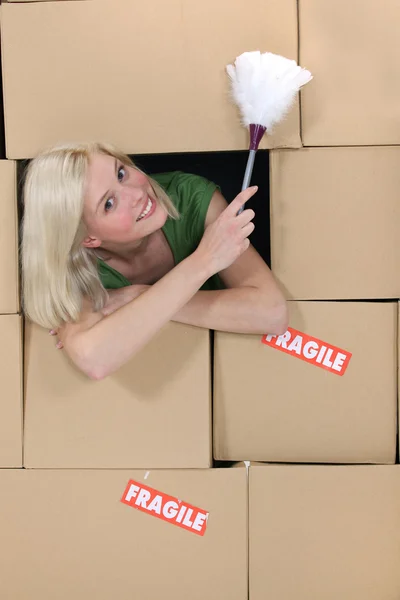 Rubia radiante en medio de cajas de cartón sosteniendo plumero — Foto de Stock