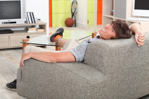 Ung man koppla av på en soffa med foten på bordet — Stockfoto