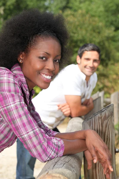 Uma mulher negra e um homem encostado à barreira de madeira — Fotografia de Stock