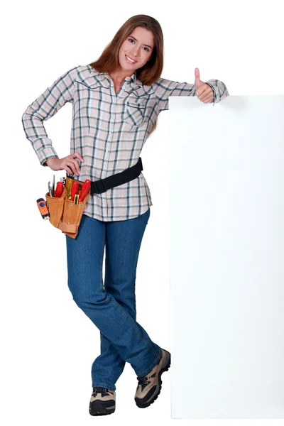 Handywoman standing next to a blank sign and giving the thumb's up — Stock Photo, Image