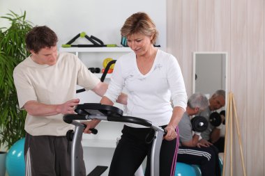 Blonde middle-aged woman on treadmill coached by physiotherapist clipart