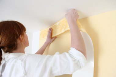 Woman putting up a wallpaper border clipart