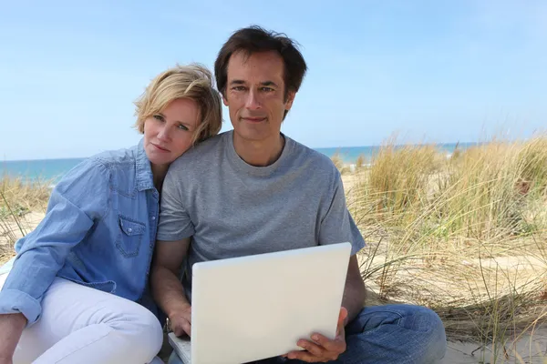Casal nas dunas usando computador portátil — Fotografia de Stock