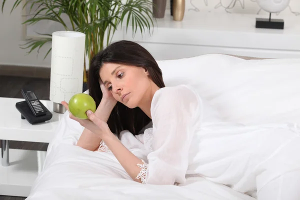 Mulher pensativa na cama assistindo uma maçã — Fotografia de Stock