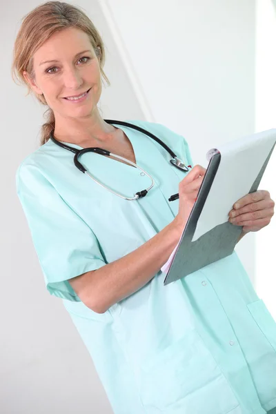 Een vrouwelijke arts schrijven op een Klembord en glimlachen op ons. — Stockfoto