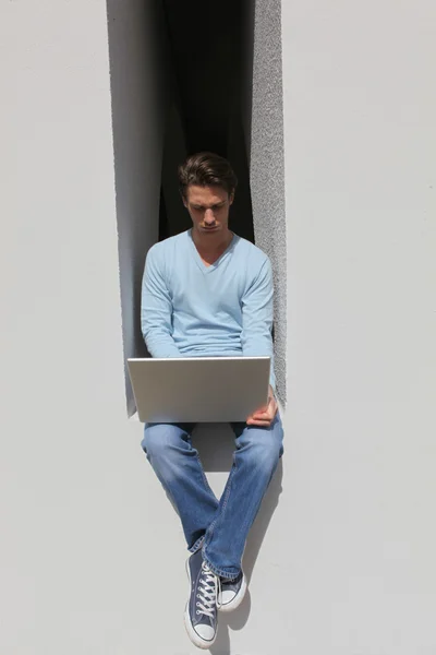 Человек сидит на низкой стене с ноутбуком — стоковое фото