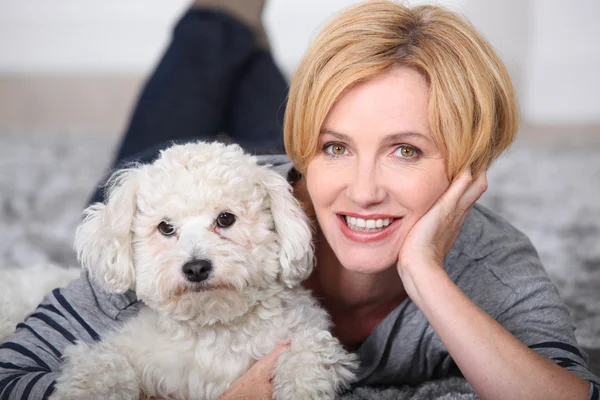 Blonde Frau liegt mit einem kleinen flauschigen weißen Hund auf dem Teppich — Stockfoto
