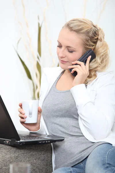 Loira no telefone trabalhando em casa com laptop — Fotografia de Stock