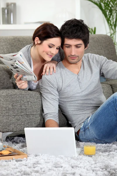 Pár seděl na gauči s noviny a laptop — Stock fotografie