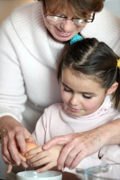 Liten flicka och hennes mormor knäcka ett ägg — Stockfoto